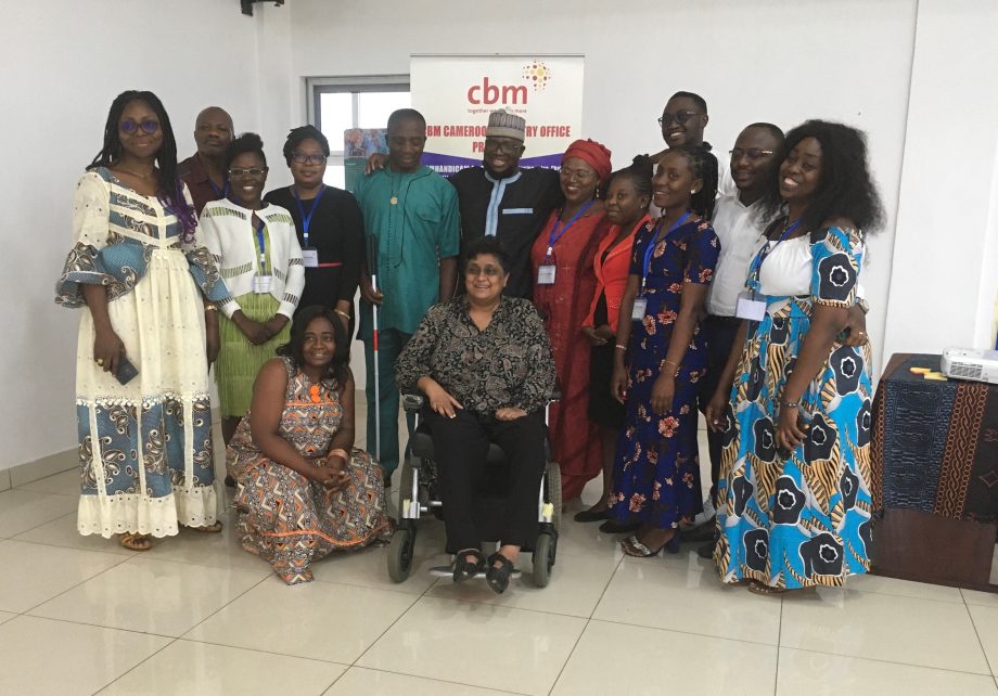 A group of people are smiling and hugging each other for a group picture. In their midst is a wheelchair user.