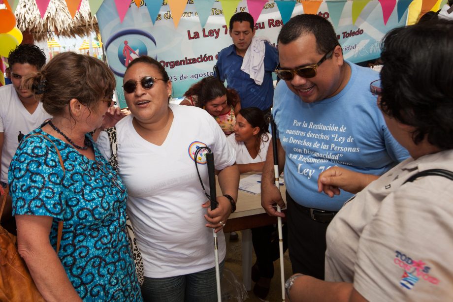 Close-up of three women and one man talking to each other while laughing. The woman and the man in the middle where sunglasses and hold canes.